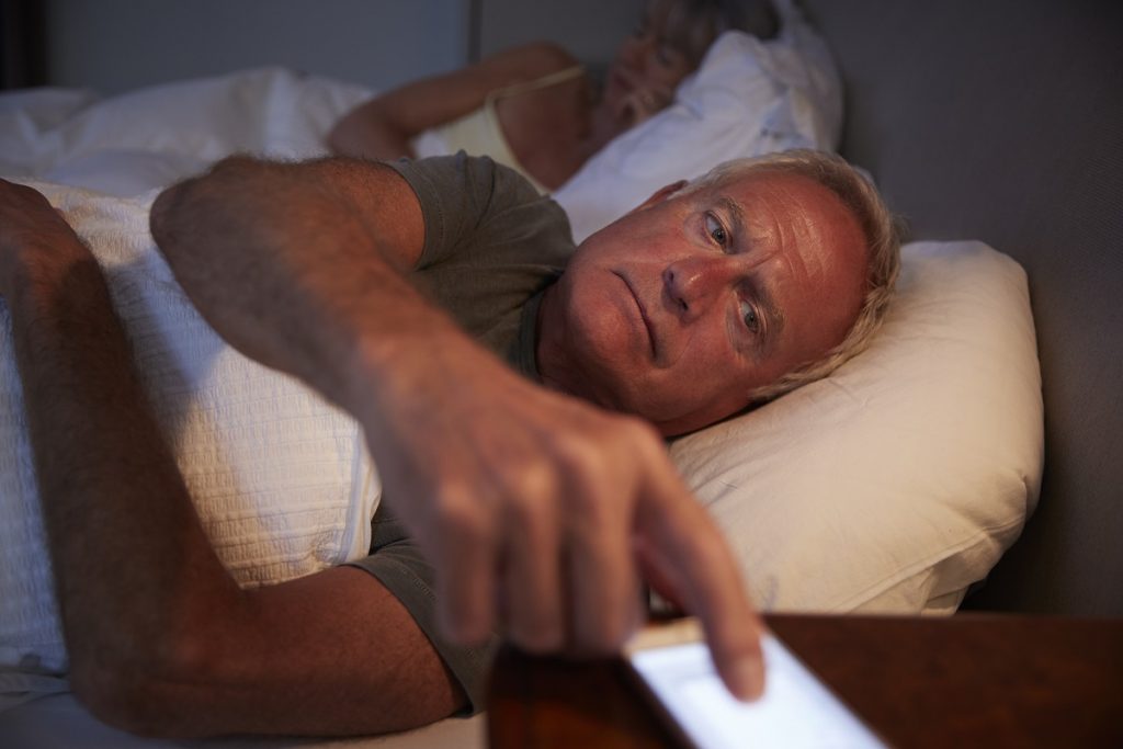 sleepless-senior-man-in-bed-at-night-checking-mobi-P9W3RED-1024x683